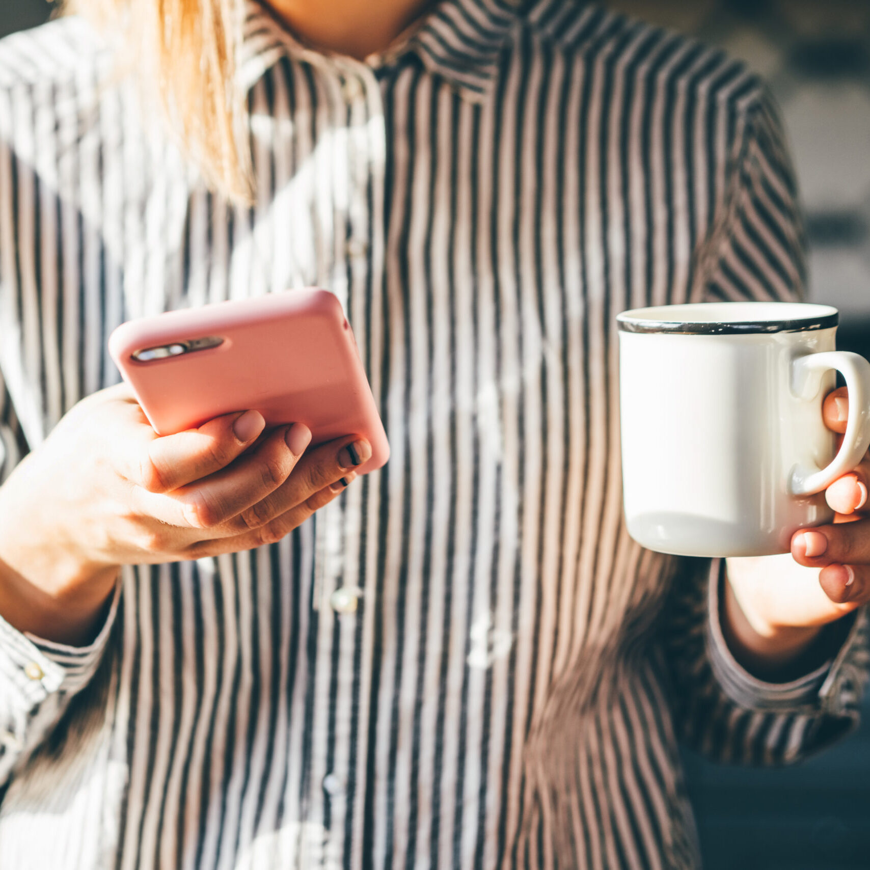 Woman holds a cup of coffe and reading news on phone at the morning.